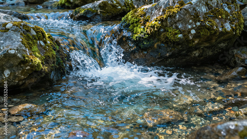 Clear stream rushes over mossy stones. Water glimmers as it tumbles gently. Rocks glow with earthy textures and green moss. Scene feels fresh and alive. Perfect for nature, travel