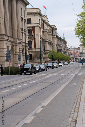 Street view in Krakow city center with historic architecture and tram tracks. People crossing the road next to classical buildings and moving traffic on a cloudy day in Poland.