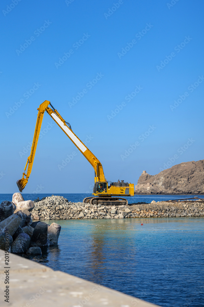 Fototapeta premium Marina development and waterfront infrastructure construction featuring excavator, stone embankment and marine engineering works