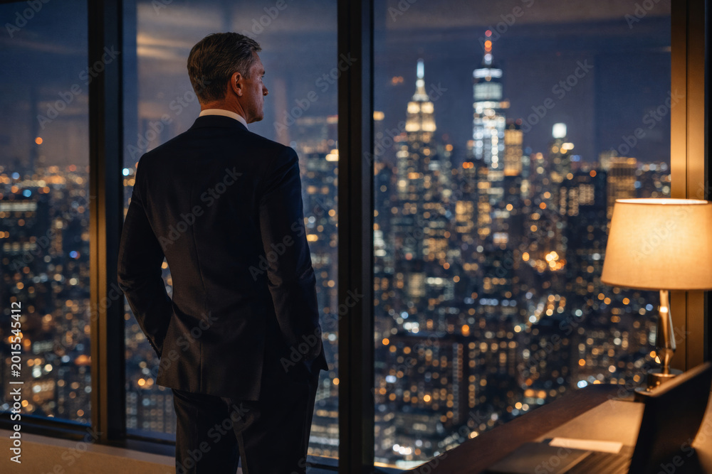Fototapeta premium Businessman overlooking city skyline at night from office