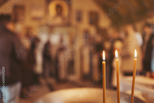 People are standing inside a place of worship. Candles are lit on a table, creating a warm glow. The atmosphere is filled with quiet conversations and reflections