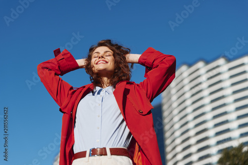 Bild auf Leinwand Cheerful woman outdoors, wearing a red jacket and white shirt, basking in sunlig