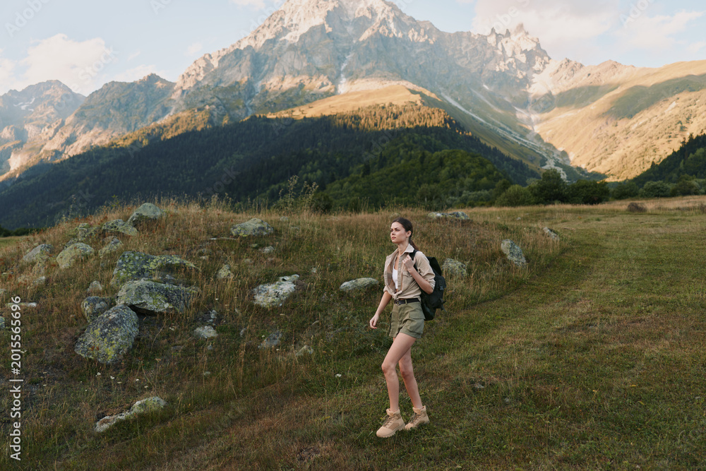 Obraz premium Woman hiker walking through a meadow beside rocky mountains, carrying a backpack, enjoying outdoor nature and expansive scenery in daylight