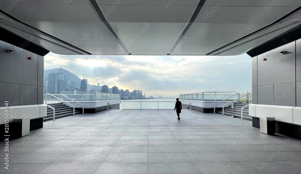 Obraz premium Lone figure walks on modern rooftop terrace overlooking city skyline and ocean