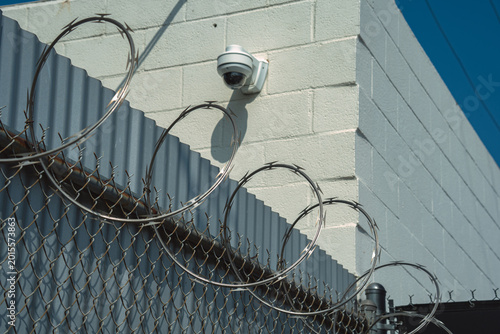 Canvas Print Security camera and razor wire fence protecting a building from intrusion