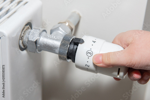 A man regulates the temperature on the radiator at home.