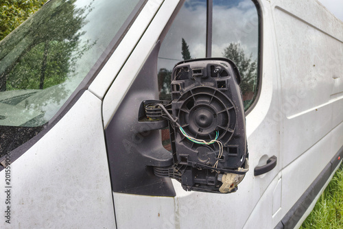 Broken side mirror on a white delivery van with exposed wiring and missing glass, parked outdoors after vehicle damage