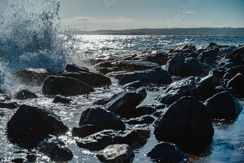 Fotografie Large wave splash over dark stones at New York beach
