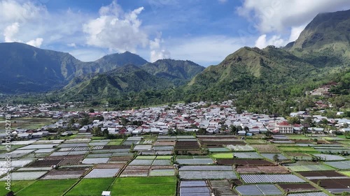 Aerial View: Idyllic Rural Village and Lush Rice Fields Nestled in a Verdant Mountain Valley Under Blue Sky