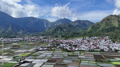Aerial View of a Picturesque Mountain Village and Extensive Farmland Under a Clear Blue Sky
