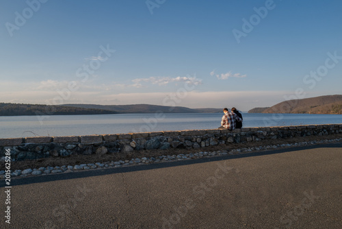 Fotografie Young couple sitting on stone wall at lake