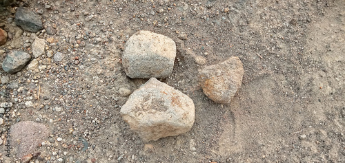 Fotografie Three natural grey stones on dry sandy ground background.