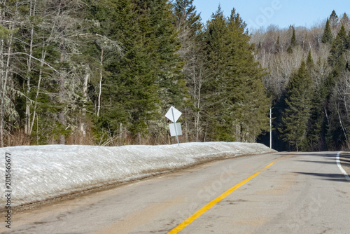 Foto Canada, 12 April 2026 : Rural road with snowbank and evergreen forest in early s