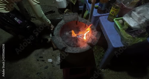 Slow motion close up of a traditional charcoal stove with bright orange flames and smoke at night.