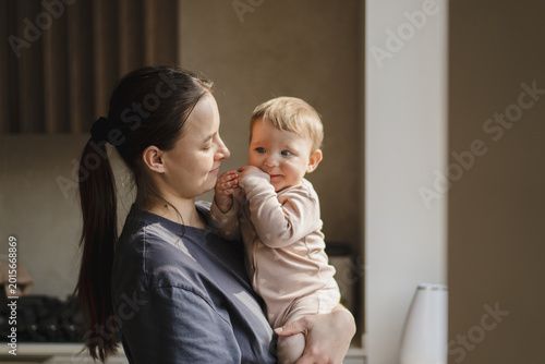 A mother is playing with her child. The sun is shining through a window, creating a warm atmosphere. Concept of baby care, early development, and healthy childhood life. Mother's Day