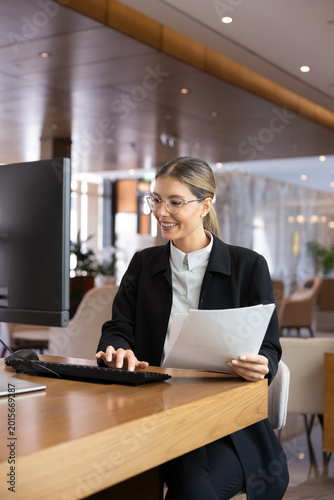 Canvas Print Female receptionist processing documents, using computer, working at hotel front