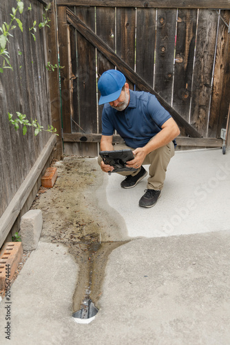 A home inspector checks and takes a pictures of a drainage on the side of a residential home