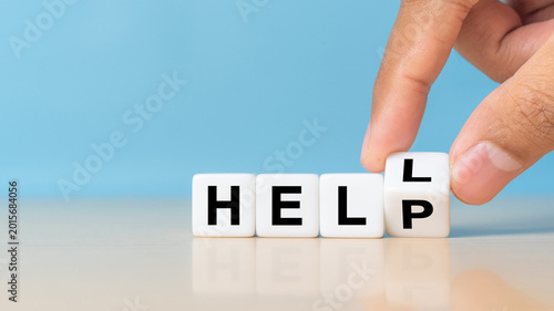 hand is flipping a cube turning the word HELL into HELP on wooden background