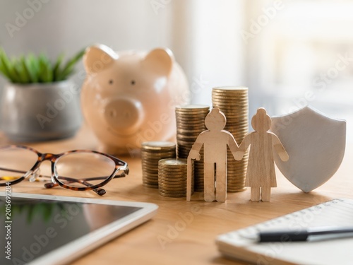Family financial protection concept with piggy bank, coins, wooden figures and shield, saving money and insurance planning
