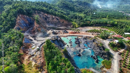 aerial view of a quarry mine surrounded by lush greenery and a vibrant blue pond.
