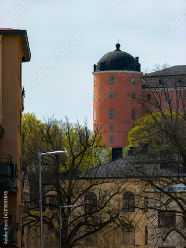 Historical orange castle tower rising above urban trees in the city of Uppsala in Sweden