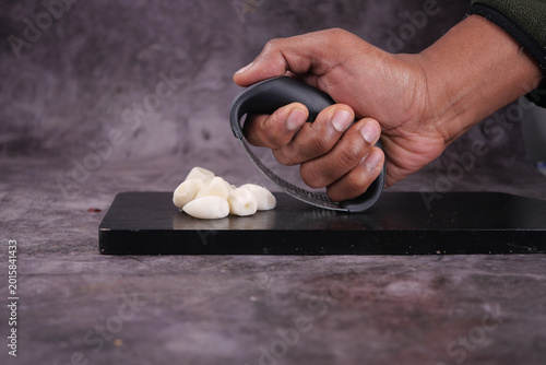 Tableau sur toile Close-up of a hand using a rocker grater to crush garlic cloves on a black cutti