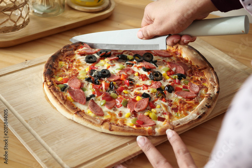 Принти на полотні Cutting pizza with toppings in a home kitchen setting