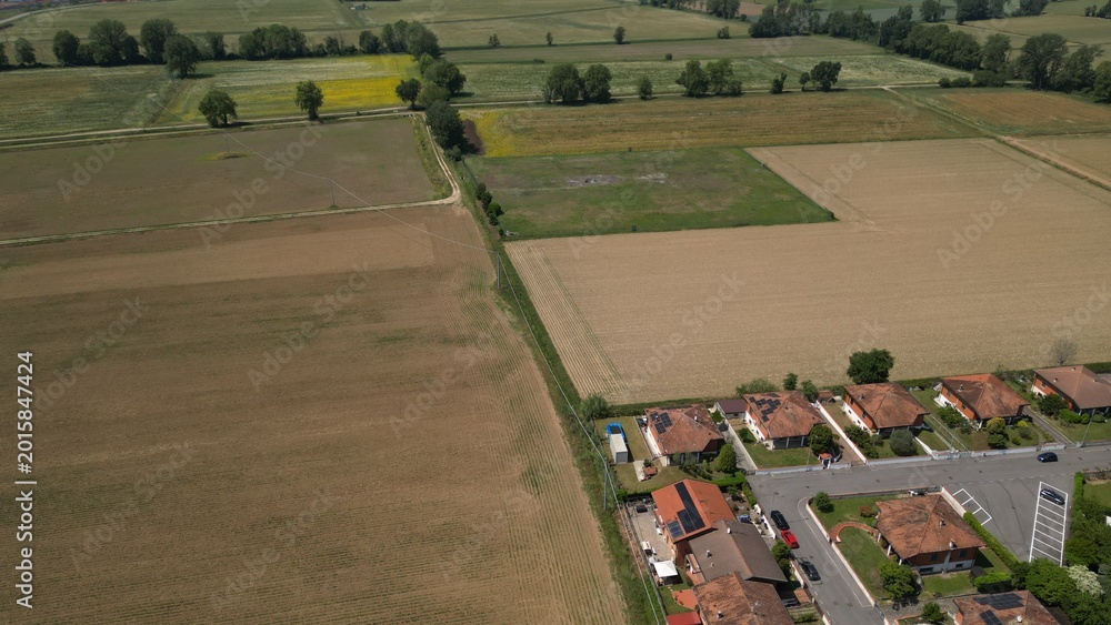Fototapeta premium Aerial Fields and Homes: An expansive aerial perspective captures a harmonious blend of rural agriculture and residential community life. This scene. Caleppio, Lombardy, Italy