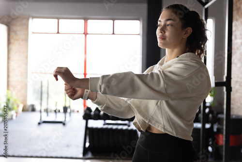 Quadro em tela Adult woman hoodie leggings stretching, adjusting watch in gym by window with pl