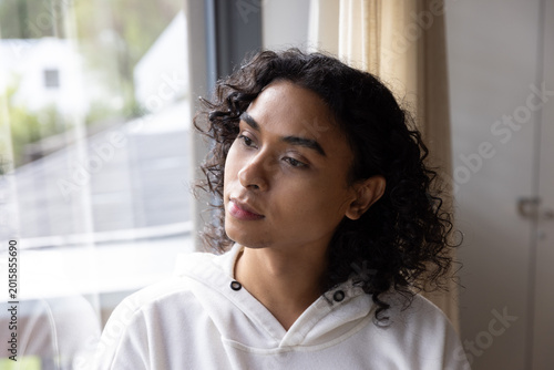 Foto Non-binary adult sitting by large window wearing white hoodie, gazing left at re