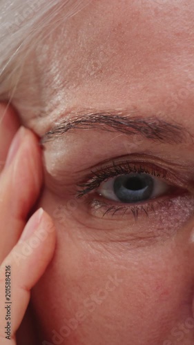 Close-up portrait: old woman face with grey hair, eyes. Concept of plastic surgery of the face, eyelid lift, blepharoplasty, cosmetology. Macro shot of senior female wrinkles near the eyes. Aging skin