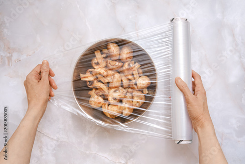 Preparing to store sliced mushrooms with plastic wrap in a kitchen setting