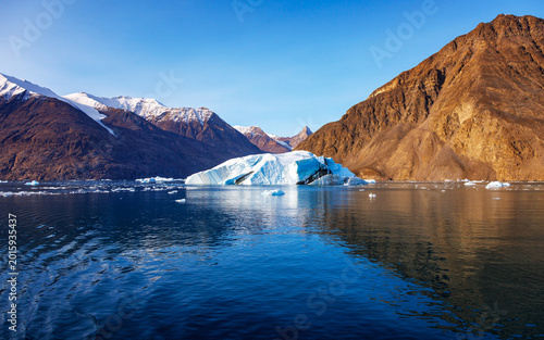 Summer landscape of blue icebergs and snow tipped mountains of Isfjord, Northeast Greenland National park, with blue sky background.