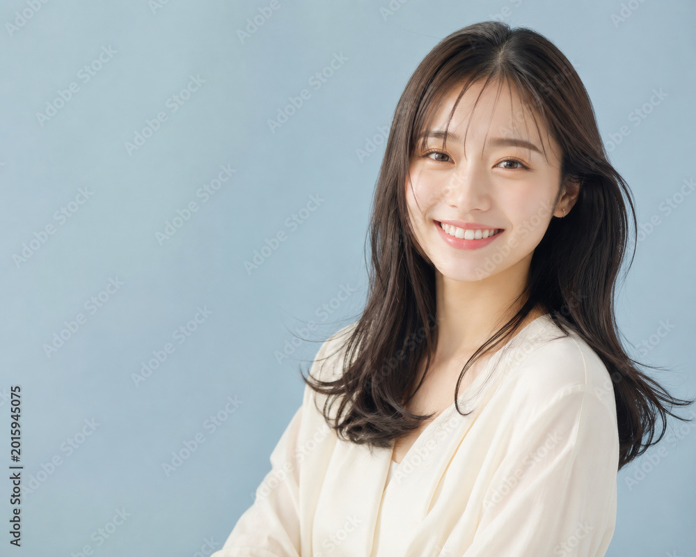 Obraz premium くすみブルー背景の前で微笑むアイボリー服の若い女性ポートレート 