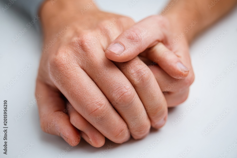 Fototapeta premium Close-up view of interlocked hands resting on a white surface, showing skin texture