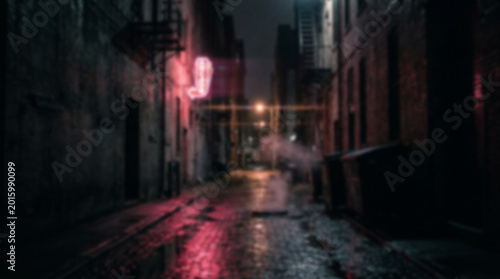 Blurred view of a dark narrow city alleyway at night with glowing red neon lights reflecting on the wet pavement