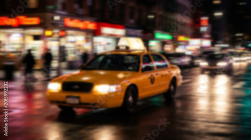 Yellow new york city taxi cab driving at night on wet street with city lights and blurred motion