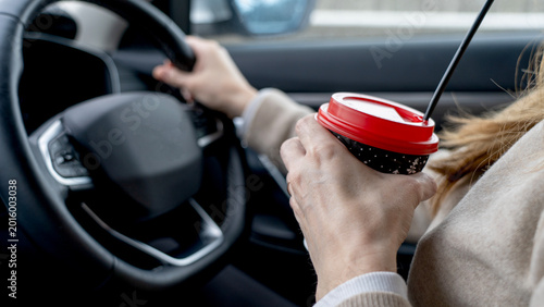 Schilderij op canvas Woman grips steering wheel, sipping coffee