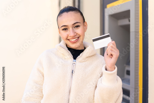 Young moroccan girl holding a credit card at outdoors with happy expression