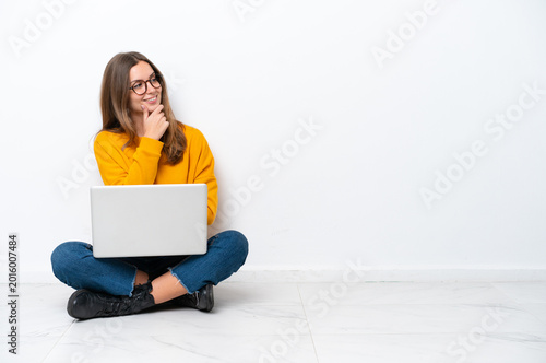 Quadro su tela Young caucasian woman with a laptop sitting on the floor isolated on white backg