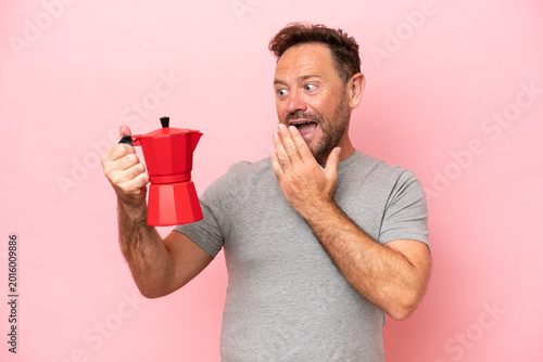 Foto Middle age caucasian man holding coffee pot isolated on pink background with sur