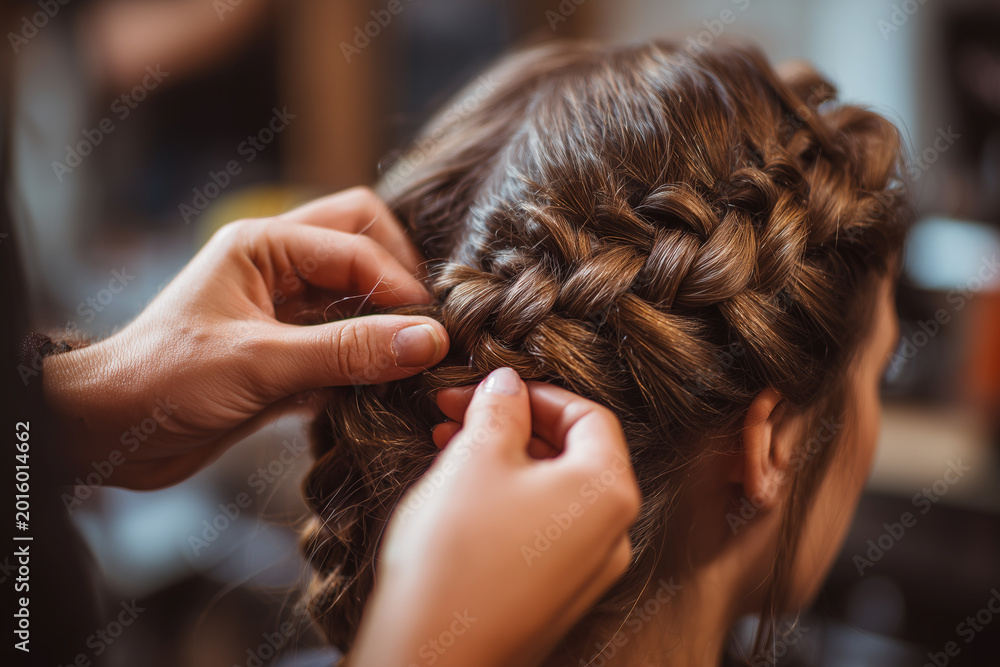 Fototapeta premium Stylist creates braids in a hair salon during the afternoon hours while working on a client's braided hairstyle with attention to detail