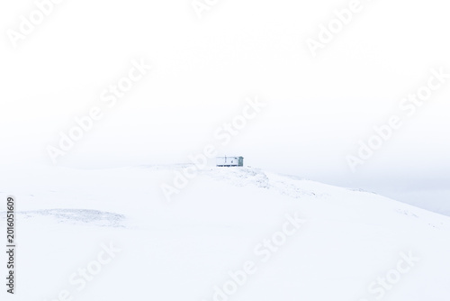 Photography Minimal cabin on a snowy Arctic Norway hillside, seen from distance in whiteout