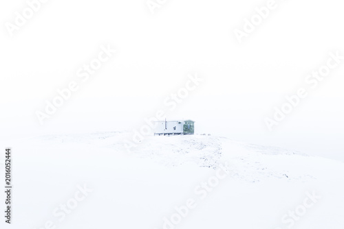 Fotografija Minimal cabin on a snowy Arctic Norway hillside, seen from distance in whiteout