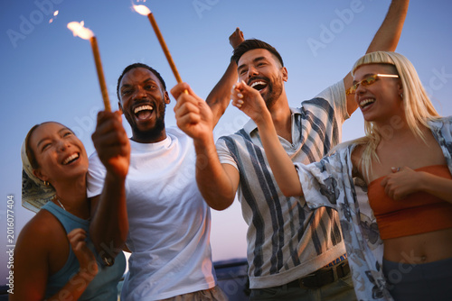 Diverse group of friends celebrating rooftop party with sparklers at sunset