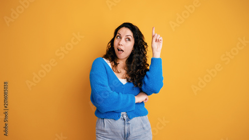 Bild auf Leinwand Curious woman finding a new solution, pointing finger up on an orange background