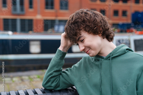 Fotografía Young person sits on bench near water in urban area, showing reflection and thou