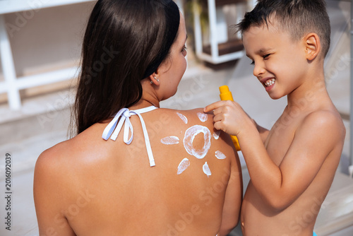 Beautiful woman enjoys sun protection while child applies sunscreen at poolside in summer setting