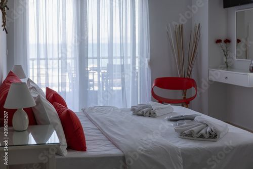Photos modern bright bedroom with red accents, white linens, and a balcony view through sheer curtains