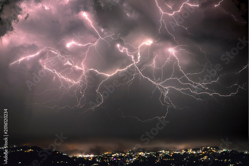 Dramatic lightning strikes illuminate a stormy night sky over a city